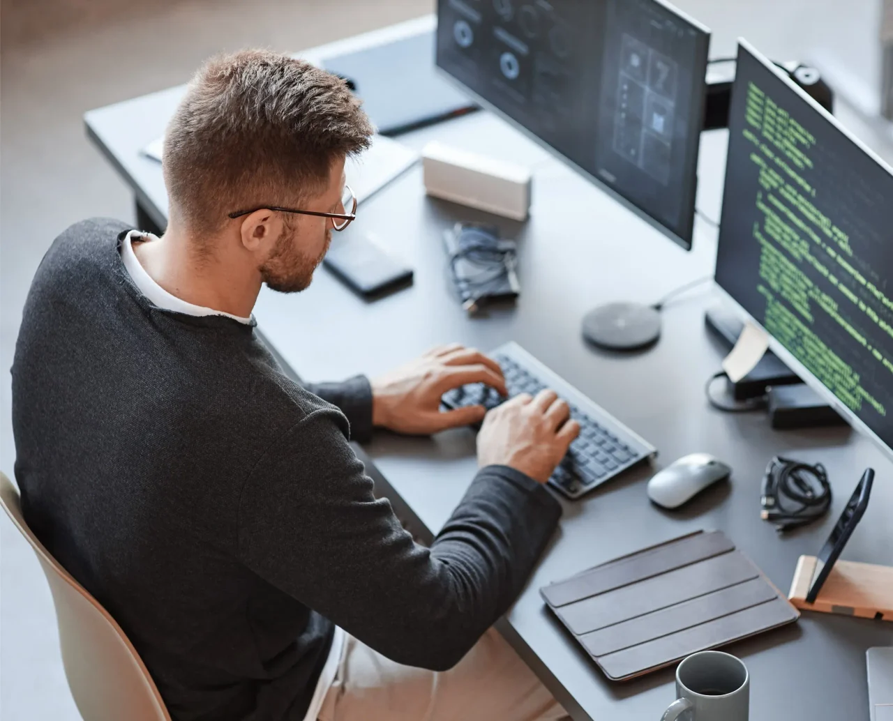 Entwickler am Schreibtisch vor zwei Bildschirmen mit Programmcode